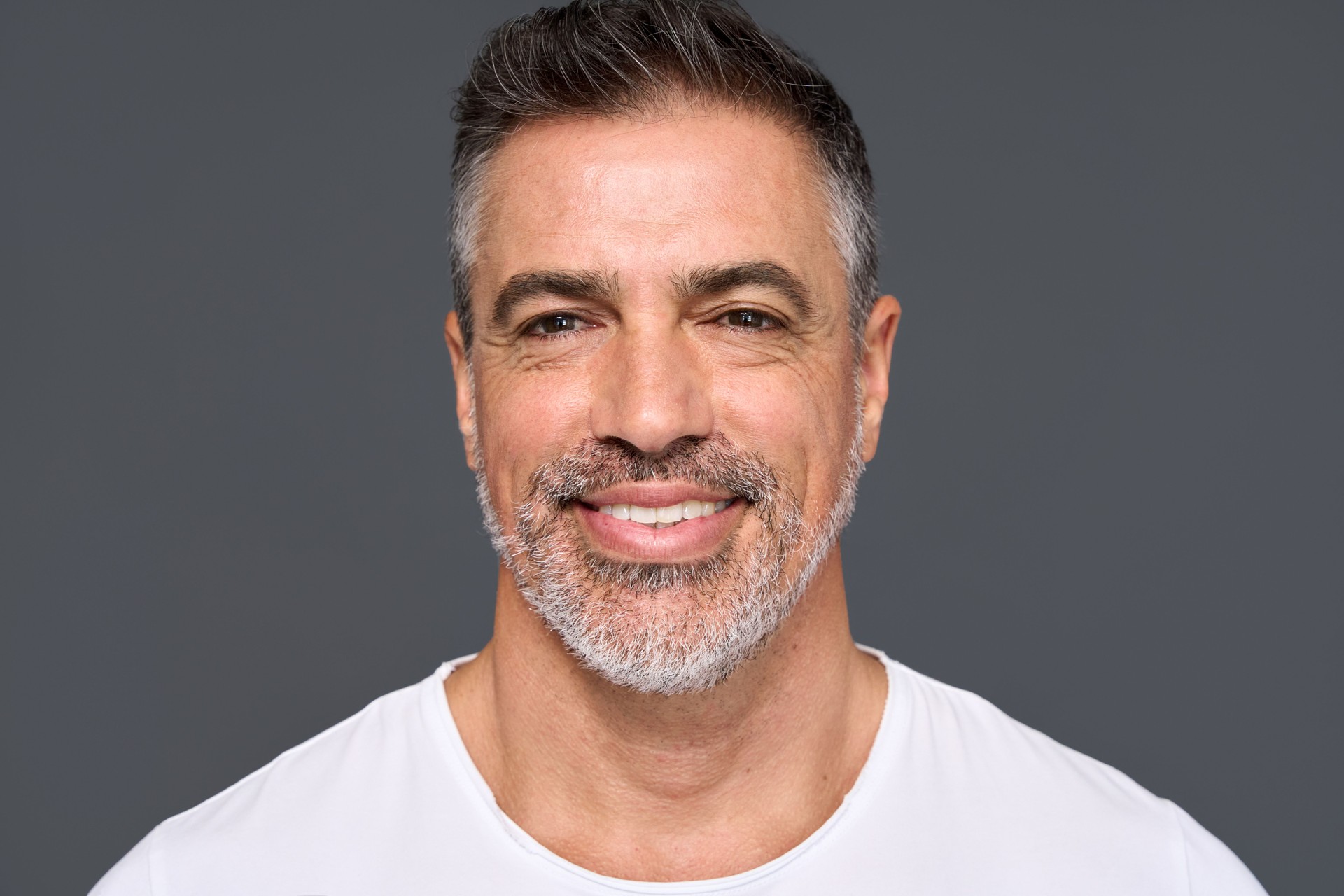 Happy mature older man wearing white t-shirt isolated on background. Portrait